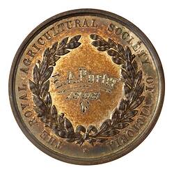 Round medal with engraved text in centre framed by wreath and raised text around edge.