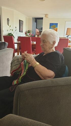 Woman sitting on couch, crocheting a striped item.
