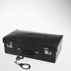 Black leather briefcase marked 'Attache Case' with handcuffs on the handle.