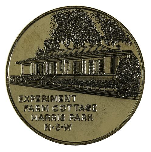 Round medal with cottage and trees.