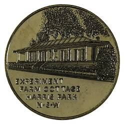 Round medal with cottage and trees.