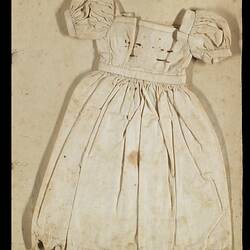 Page of an unbound book with a sewing sample of a white short sleeved doll's dress.