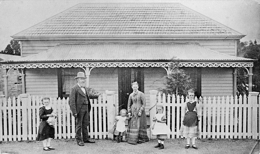 Family of 6 in front of house with a picket fence.