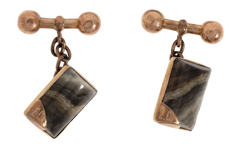 Rectangular rose gold cufflinks, each with a striped grey stone. Set in rose gold with chain attached to dumbbell-shaped toggle. Initials in gold-tipped corner.