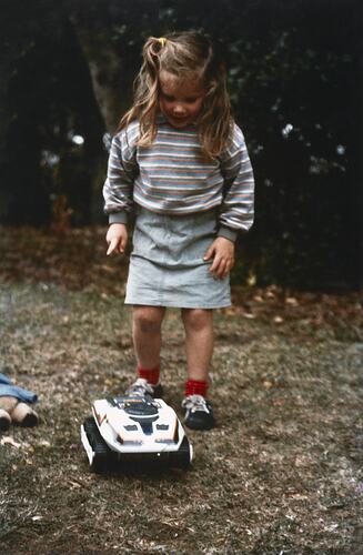 Young girl playing outside with large toy car.