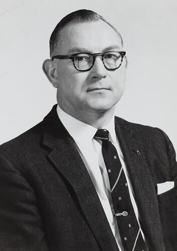 Portrait of man wearing suit, tie and glasses.