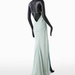 Back view of full length pale green silk evening slip dress. Sleeveless. Fastens at back with long green silk covered rope ties. Flared/fishtail skirt.