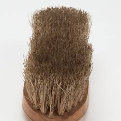 Oval shaped light brown wooden brush with off-white bristles. End view.