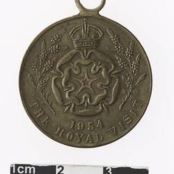 Round medal with floral motif in centre and crown above, surrounded by wreath and text.
