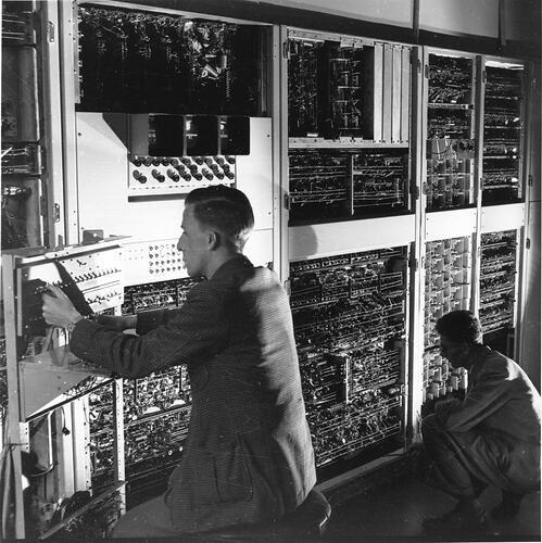 Two men in front of banks of circuitry.