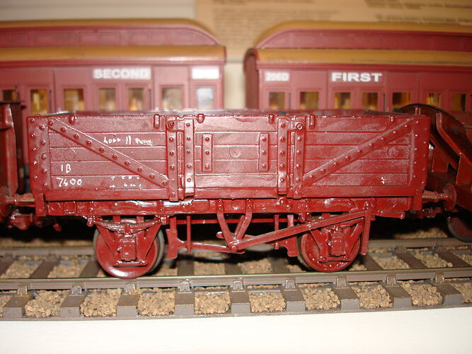 Rectangular, open-top model railway carriage. Moulded brown plastic frame with metal undercarriage and wheels.