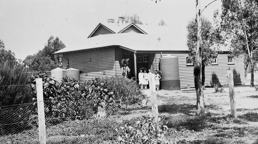 Exterior view of a school made of corrugated iron with students standing in the entrance doorway.