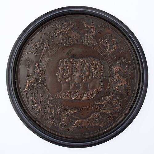 Round medal with four overlaid male profiles facing left. Battle scene around them.
