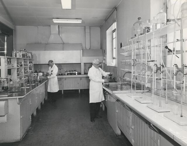 2 men in white coats, standing at laboratory work bench.