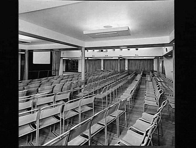 Ship interior. Room with metal chairs set up in rows to create cinema seating.