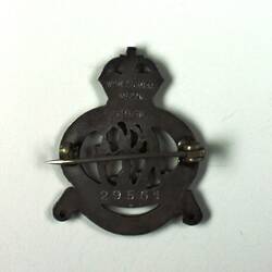 Back of grey metal badge with fastening pin and stamped text.