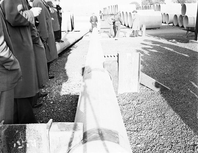 Monochrome photograph of men testing cement pipes.