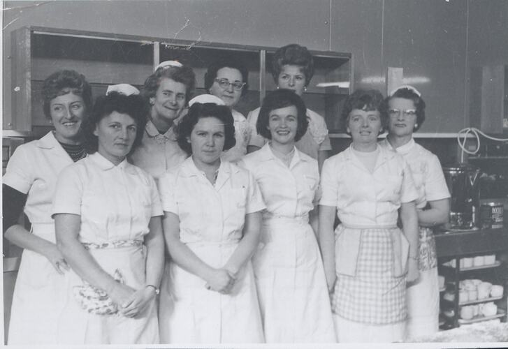 Eight women in uniform in kitchen.