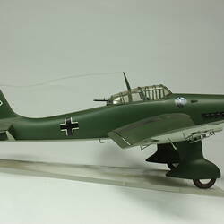 Model aeroplane. Dark green with black cross on tail. Black propeller and wheels. Right profile.