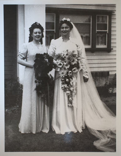 Bride and bridesmaid in front of house.