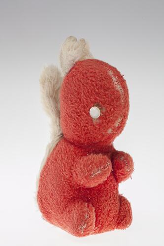 Right view of red plush toy squirrel with two white button eyes, white ears and tail.
