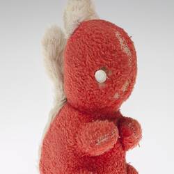Right view of red plush toy squirrel with two white button eyes, white ears and tail.