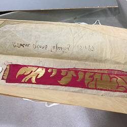 Tapestry laying in paper wrapping with inscription.