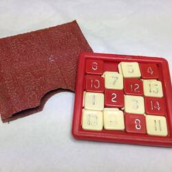 Red and white square tile plastic puzzle game with cloth red pocket.
