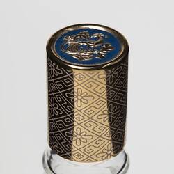 Perfume bottle gold plastic lid with geometric design. Lid top has gold bird on blue.