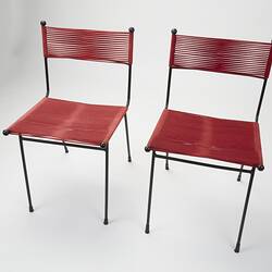 Two metal chairs strung with red cord seats and back sections. Top left view.