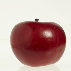 Wax model of an apple with stem, painted dark red, with brown stem.