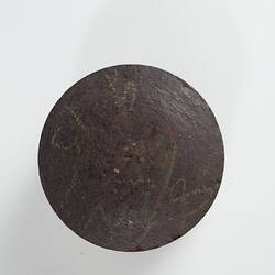Disc-shaped dark brown briquette with flat sides. Top view.