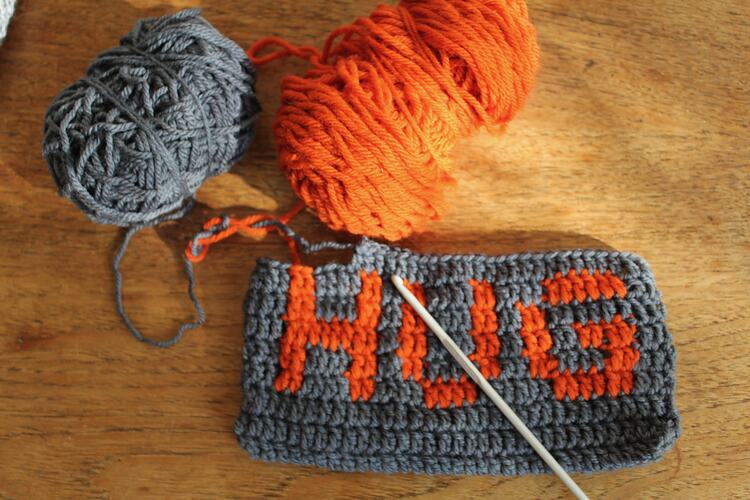 Crochet piece reading 'HUG' with two yarn balls.