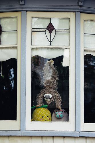 Toy sloth placed upside down in window.