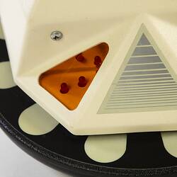 Detail of base of cream plastic robot with angular human-like shape, ie. head, shoulders, waist and legs. Black plastic features.