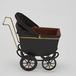 Painted black metal miniature pram with gold painted highlights and folding leather hood. Right profile.