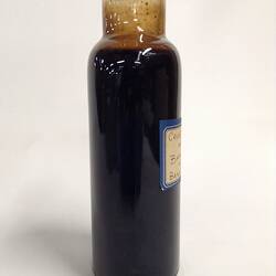 Side view of dark glass jar containing crude oil sample. Off white label has handwritten text.