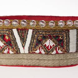 Side view of red fabric crown decorated with clear beads and trimming.