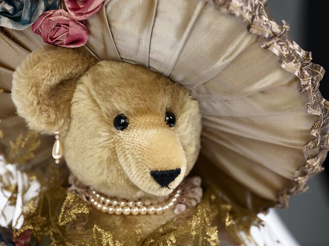 Detail of light brown teddy bear wearing lavish cream hat.
