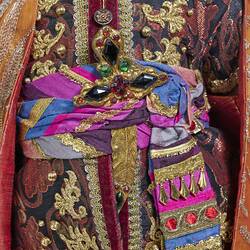 Detail of bejewelled ornate burgundy tunic gold embroidery and blue purple belt.