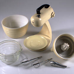 Cream metal food mixer with two bowls and parts around.