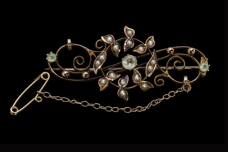 Central gold circle of seed pearls overlaying gold scroll with three paste stones. Fine chain and pin at right.