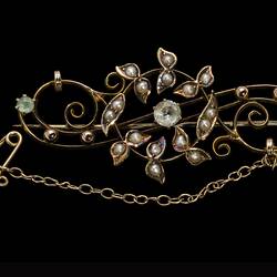 Central gold circle of seed pearls overlaying gold scroll with three paste stones. Fine chain and pin at right.