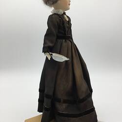 A doll dressed in a dark brown dress with a cameo brooch