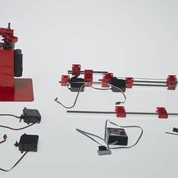 Red and black plastic components with cables that make up a toy robotic arm.