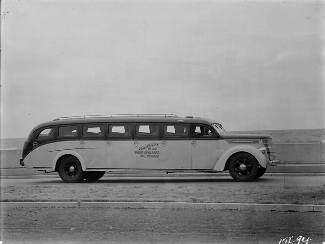 Two-toned motor bus with grass in foreground, water (ocean?) in background.