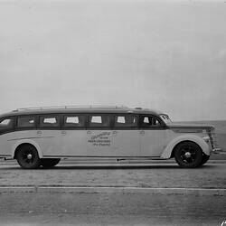 Two-toned motor bus with grass in foreground, water (ocean?) in background.