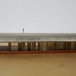 Model of a house with an arched roof, corrugated iron and wide expanses of glass.