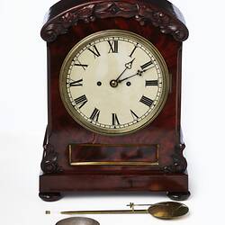 Mantel clock with white face and roman numerals. Mahogany case. Parts laid out in front.