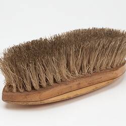 Oval shaped light brown wooden brush with off-white bristles.